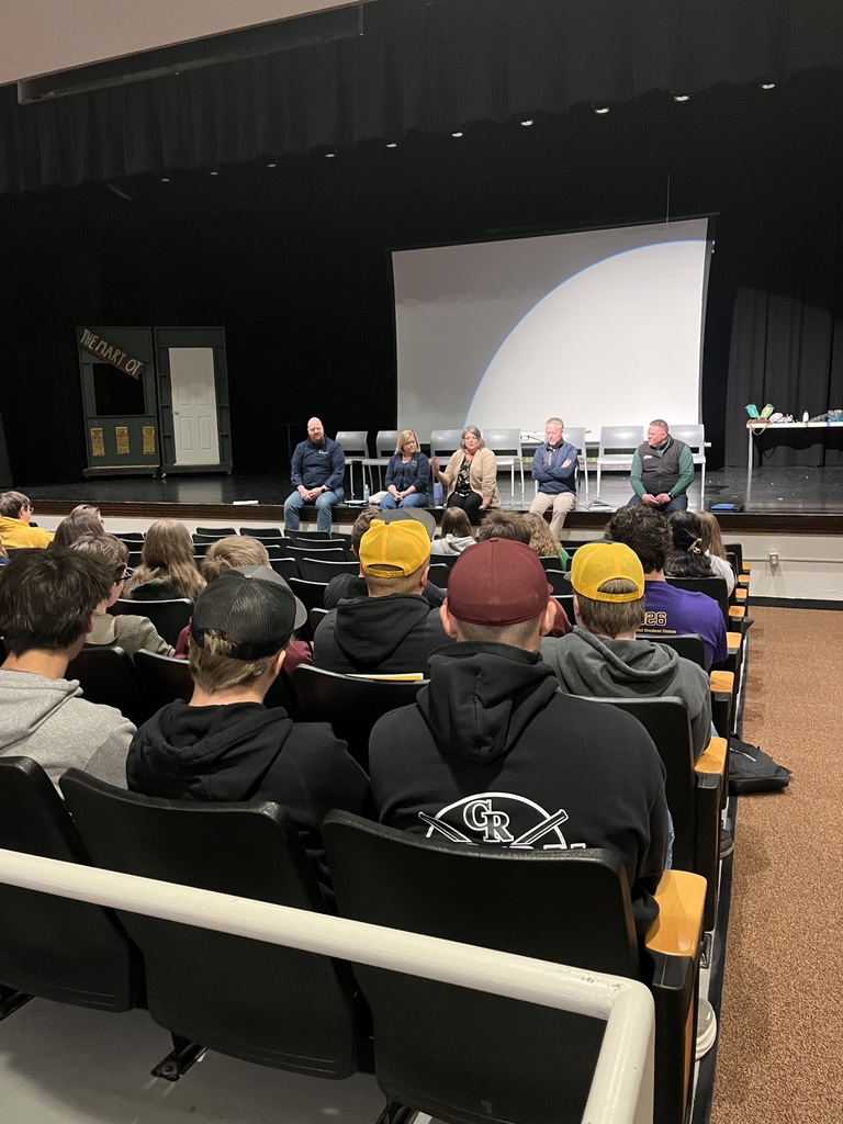 panel of speakers on auditorium stage in front of high school students