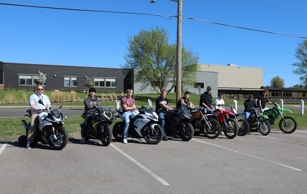 8 students and 1 teacher sitting on motorcycles that they drove to school
