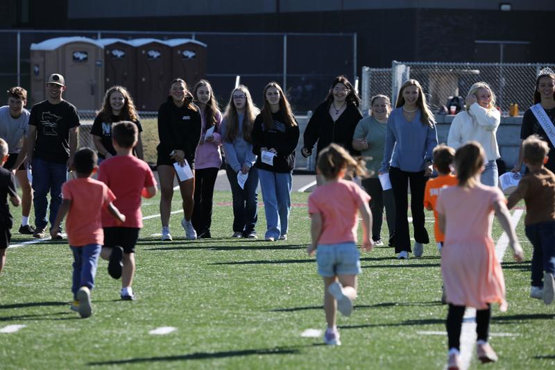 Kindergarten students running towards seniors on the football field