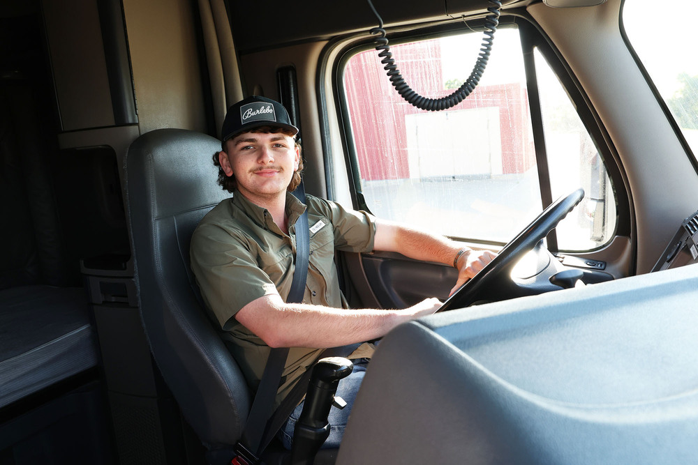 young man buckled in the driver seat of a semi truck with his hands on the wheel