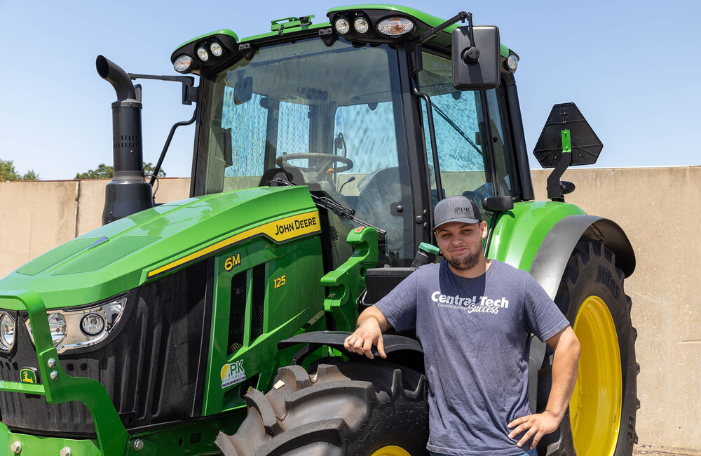 adult student Kyle Adair stands in front of a John Deere tractor wearing a Central Tech t-shirt