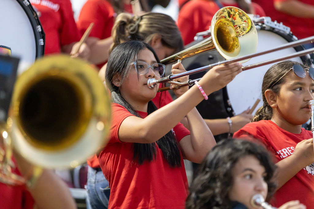 Girl surrounded by fellow student musicians - all in red t-shirts - plays slide trombone.
