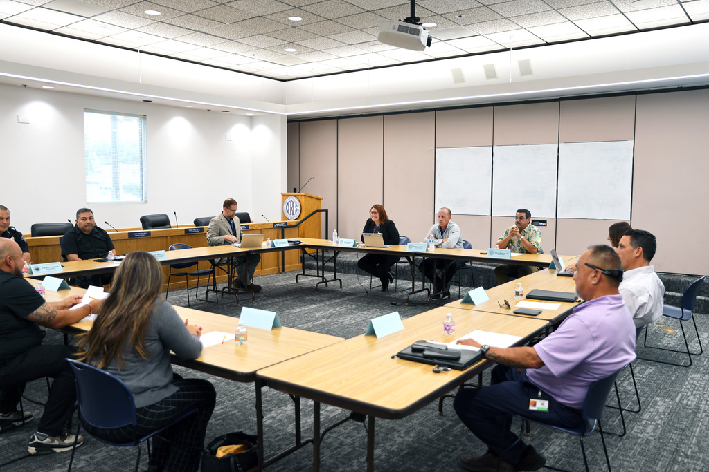 School and district leaders seated around tables in conference room.