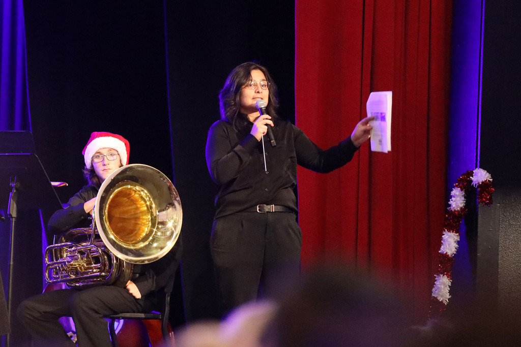Music Director on stage holding mic with tuba player in background