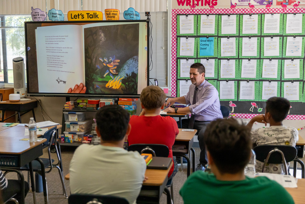 A man reading a book to a classroom full of students