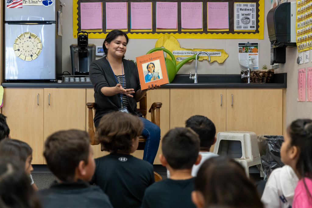 A woman reading a book to a classroom full of students