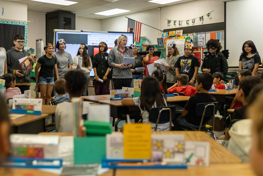 A group of students and one adult talking to a classroom full of students