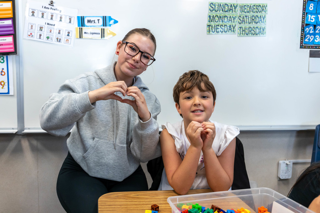 Staff and student giving a heart hand motion