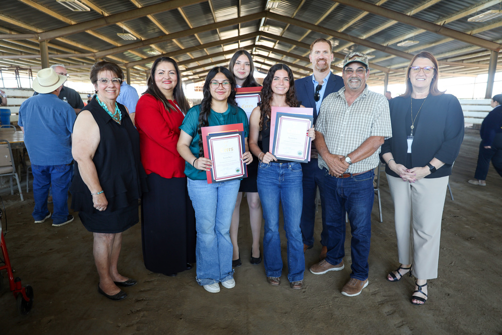 Three students holding certificates and flanked by Board members and district Superintendent, Deputy Superintendent