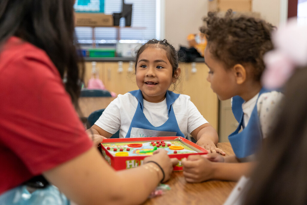 Smiling kindergarten student plays a board game with classmate and teacher