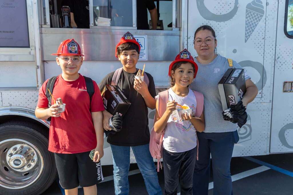 Three students wearing fire hats and holding frozen yogurt pose with parent