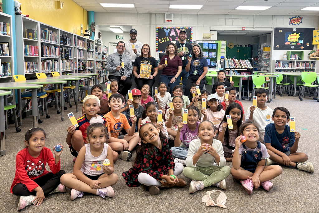 Large group of young students sitting cross-legged on floor holding bookmarks and squishies
