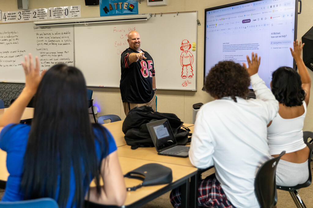 teacher pointing at a group of students raising their hands