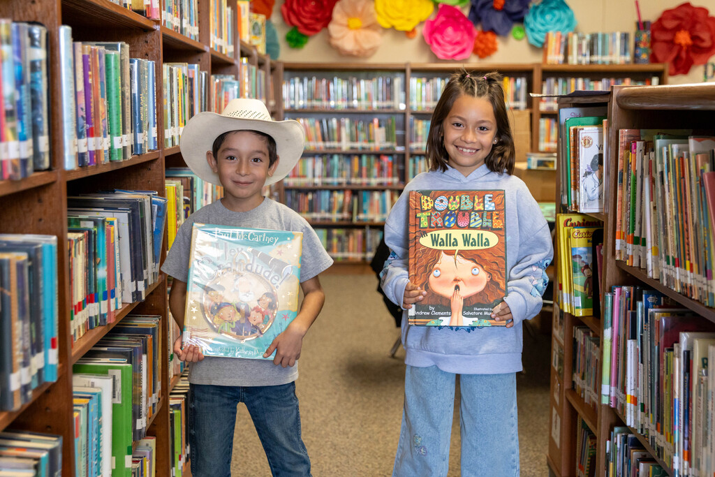 two students holding books in a library