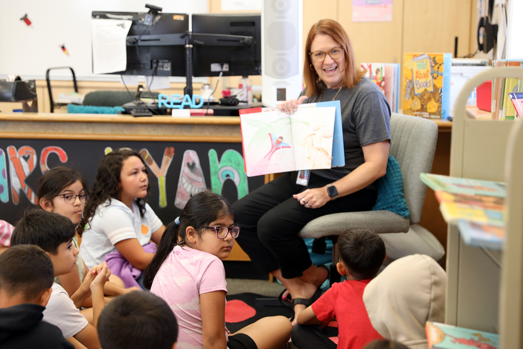 Superintendent shows pictures in book she is reading to students seated on floor