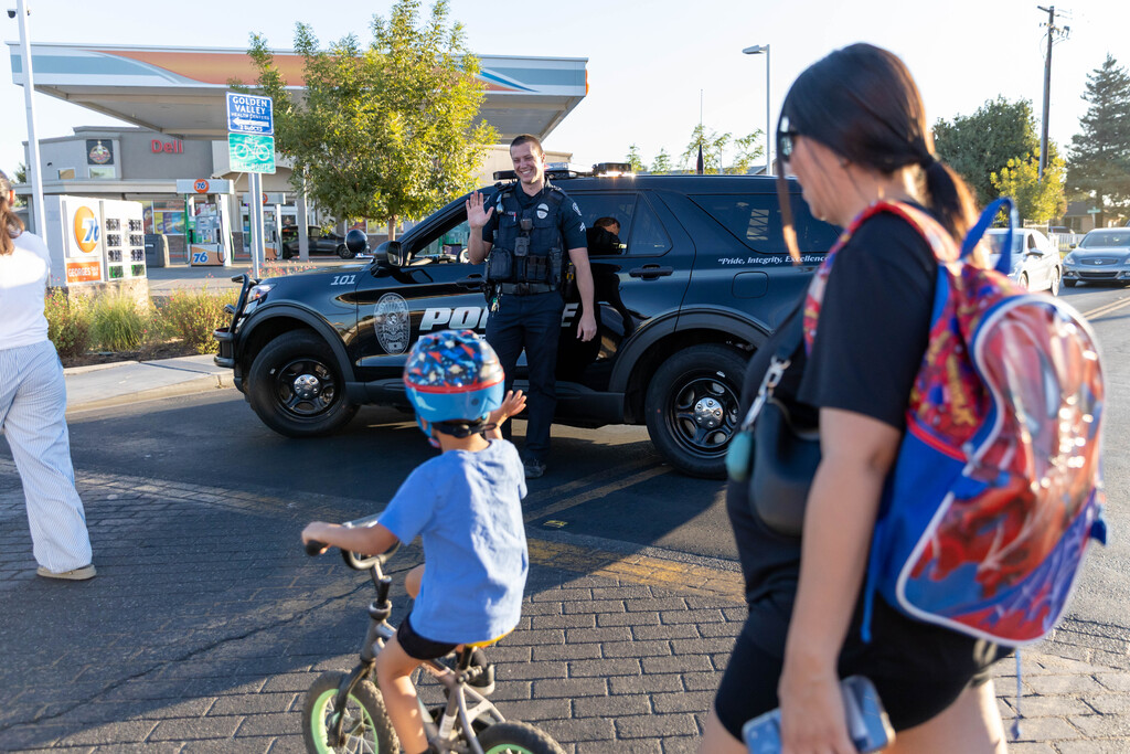 student on a bike waving to a police officer