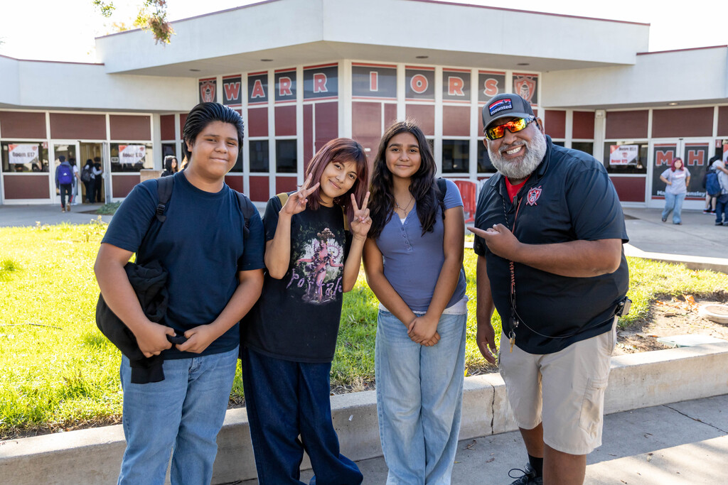 Three students and staff member in front of school