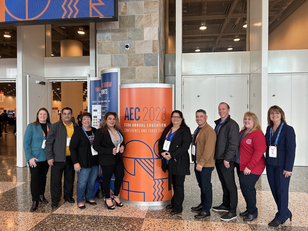 Board members and staff stand in front of building with orange conference sign