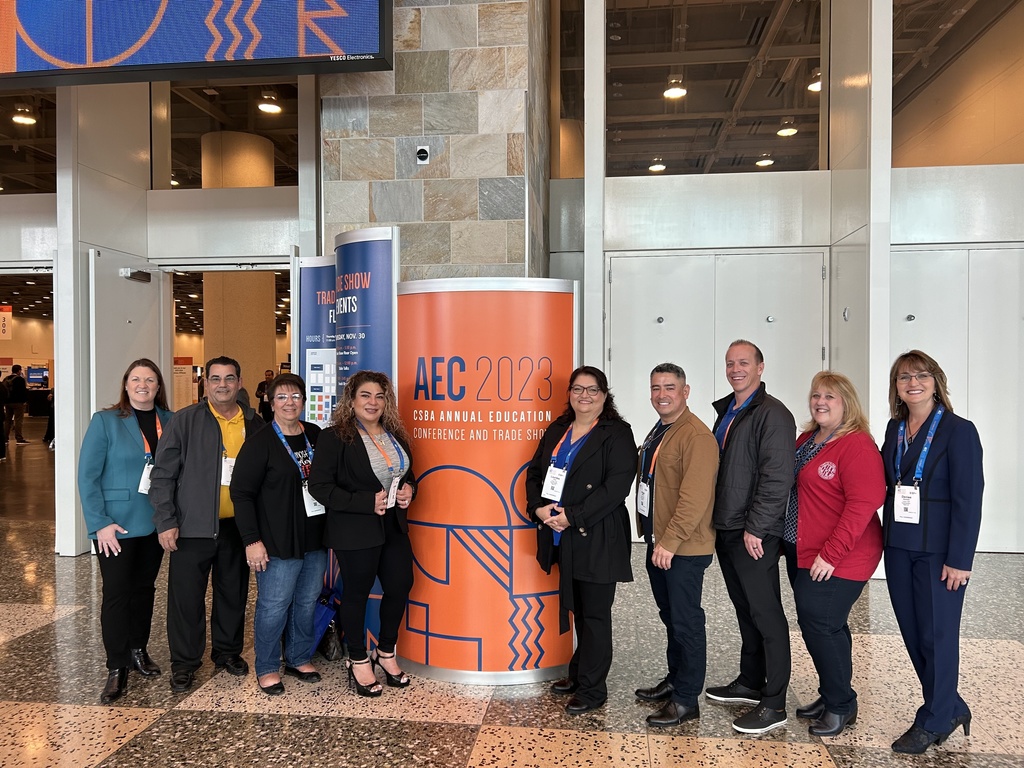 Board members and staff  stand in front of building with orange conference sign