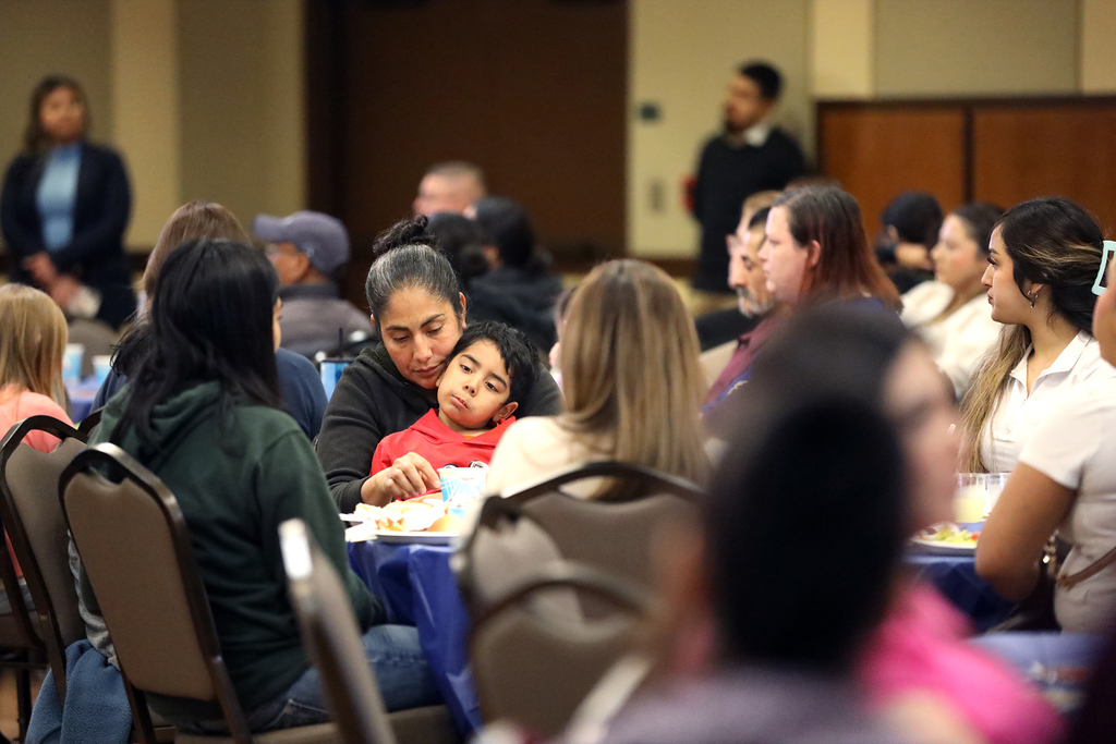 Audience members, including woman holding child in lap, listen to speaker