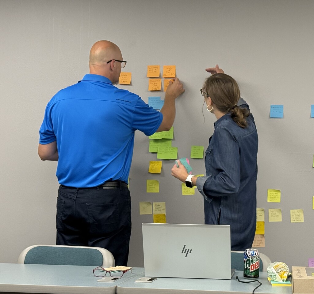 Dean Leisgang and Aly Tress working on process mapping by putting sticky notes on a wall.