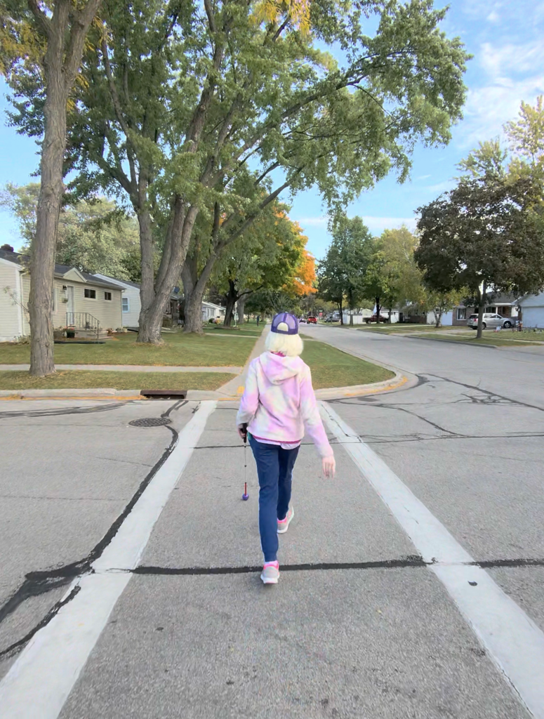 A visually impaired student walking with a cane through a crosswalk.