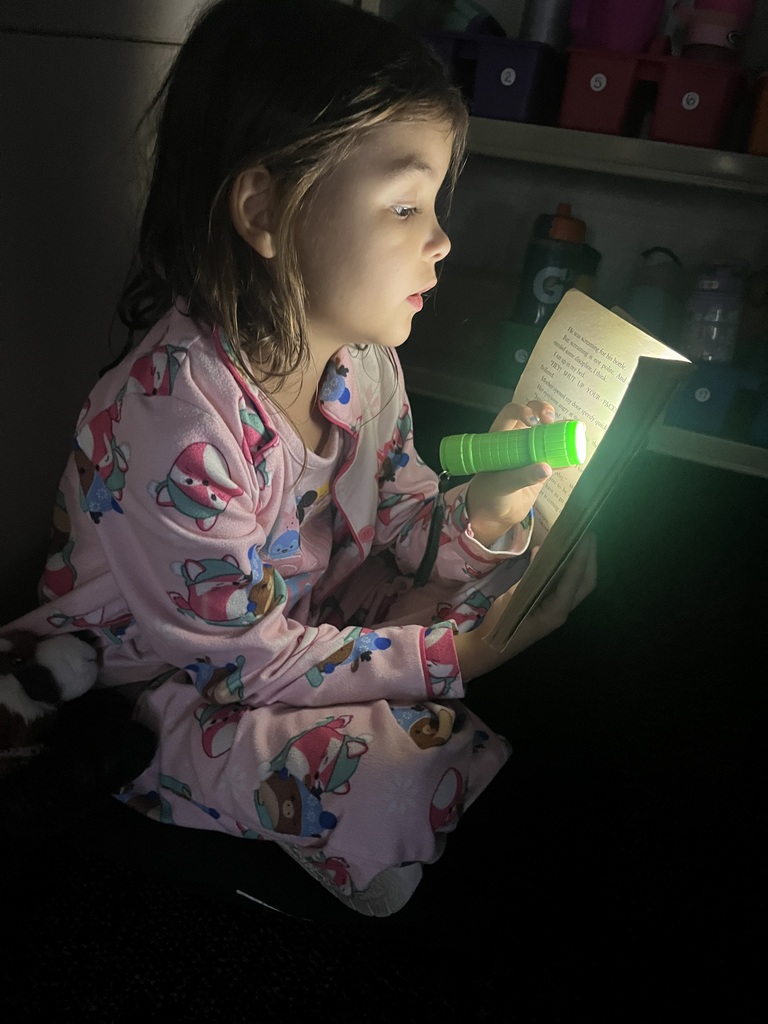 Students reading books using flashlights.