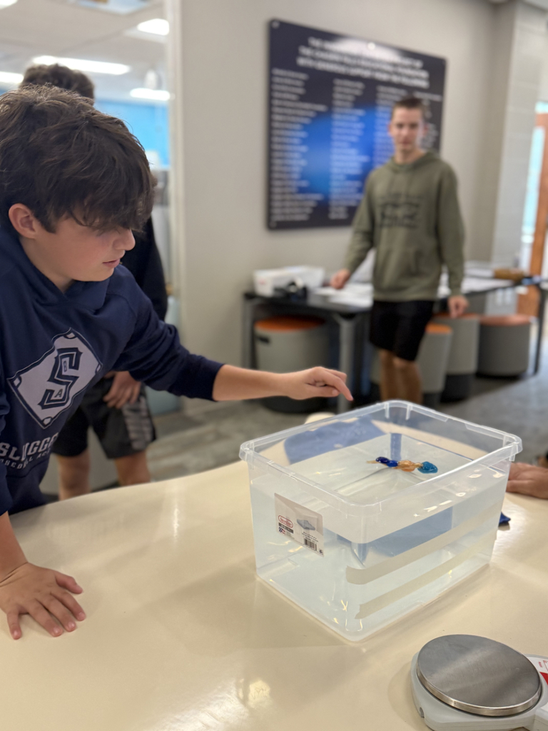 Using hot glue, students experimented with items like beads, hardware, popsicle sticks, and balloons to adjust balance and achieve neutral buoyancy.