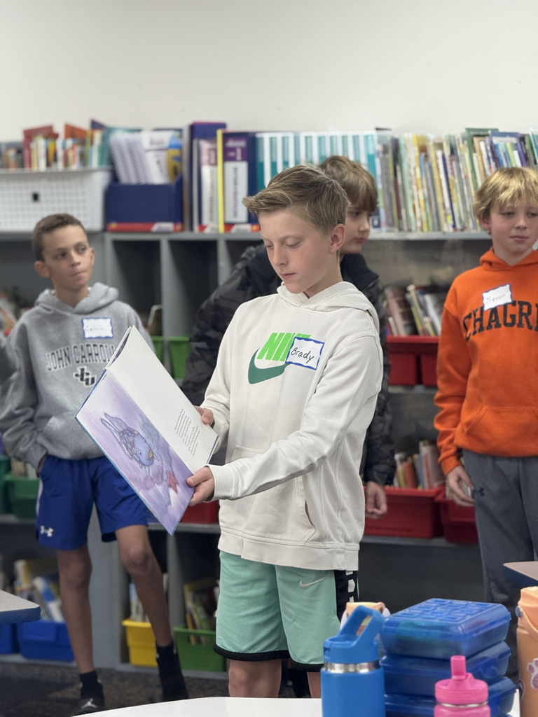 Sixth grade students sit beside first graders, helping them create Rainbow Fish art projects after reading the book together in Mr. Wise’s classroom.