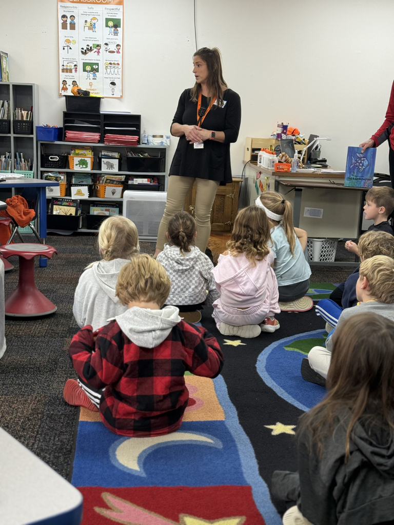 Sixth grade students sit beside first graders, helping them create Rainbow Fish art projects after reading the book together in Mr. Wise’s classroom.