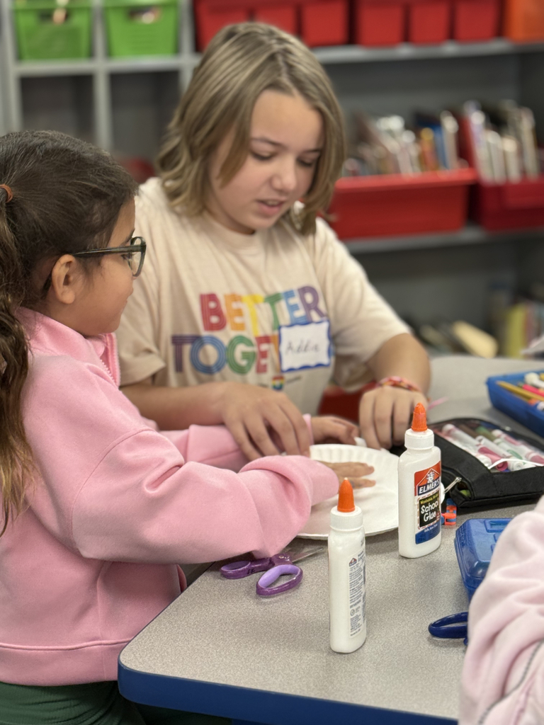 Sixth grade students sit beside first graders, helping them create Rainbow Fish art projects after reading the book together in Mr. Wise’s classroom.