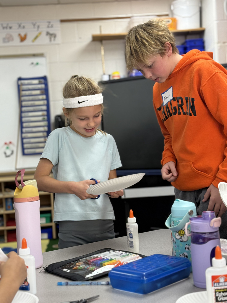 Sixth grade students sit beside first graders, helping them create Rainbow Fish art projects after reading the book together in Mr. Wise’s classroom.