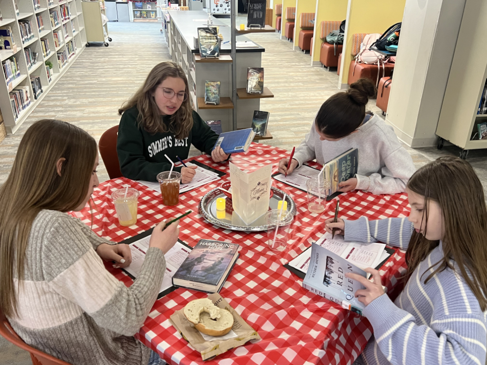 Middle school students sit at decorated tables in the Innovation Center, transformed into the IC Cafe, sampling books, taking notes, and enjoying drinks while exploring a variety of high interest titles.