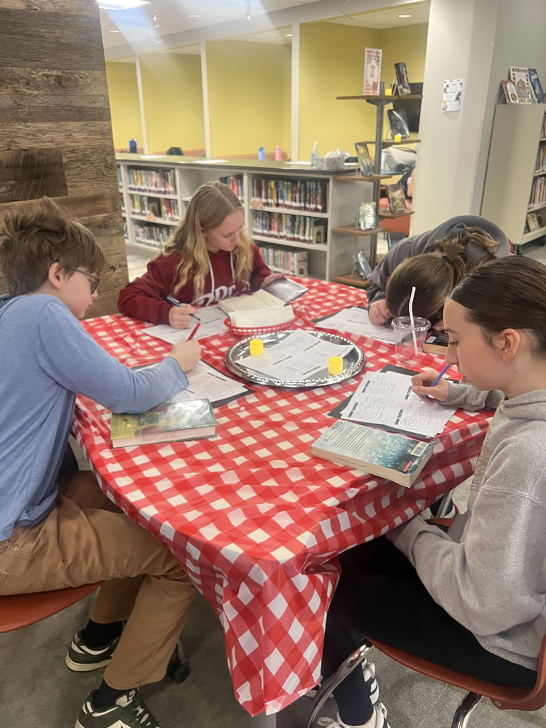 Middle school students sit at decorated tables in the Innovation Center, transformed into the IC Cafe, sampling books, taking notes, and enjoying drinks while exploring a variety of high interest titles.