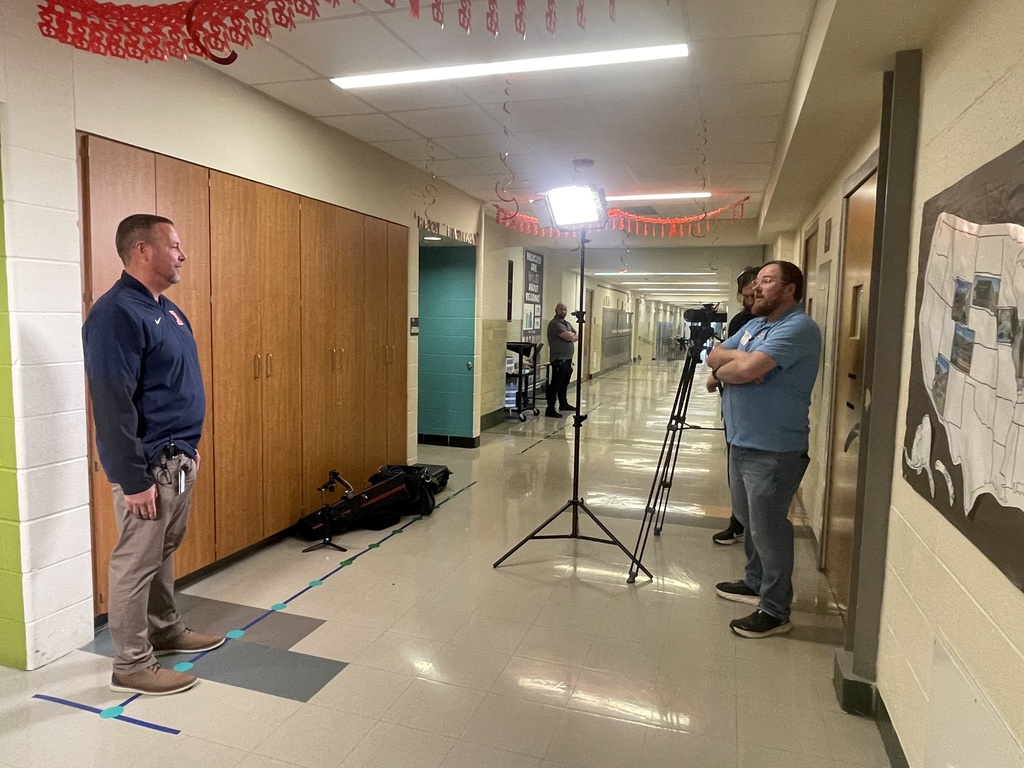 Three people in a hallway with walls painted in blue, green, and yellow. A man with a camera on a tripod.