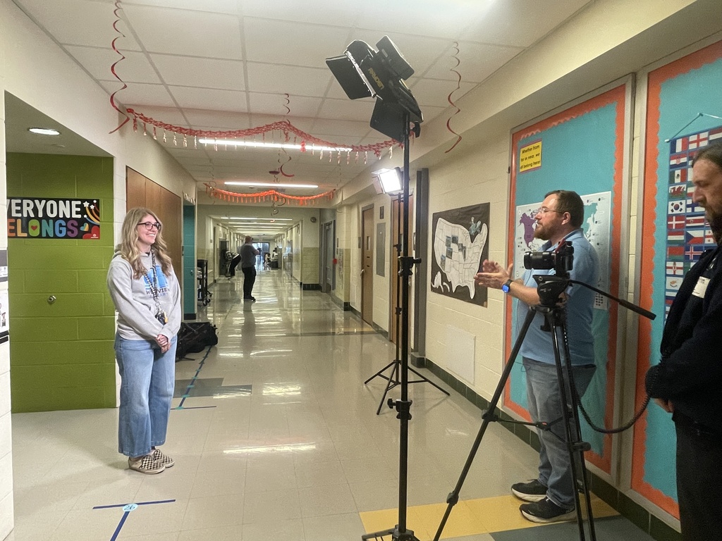 Three people in a hallway with walls painted in blue, green, and yellow. A man with a camera on a tripod.