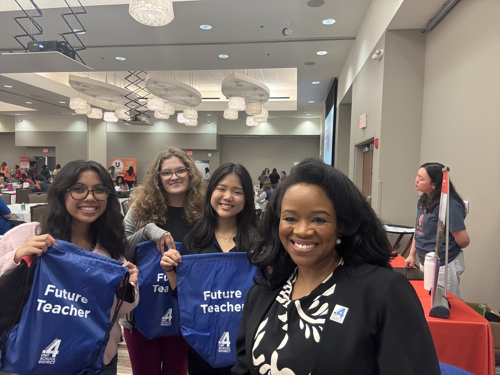 Four women with bags that say "Future Teacher" pose for a picture in a large room.