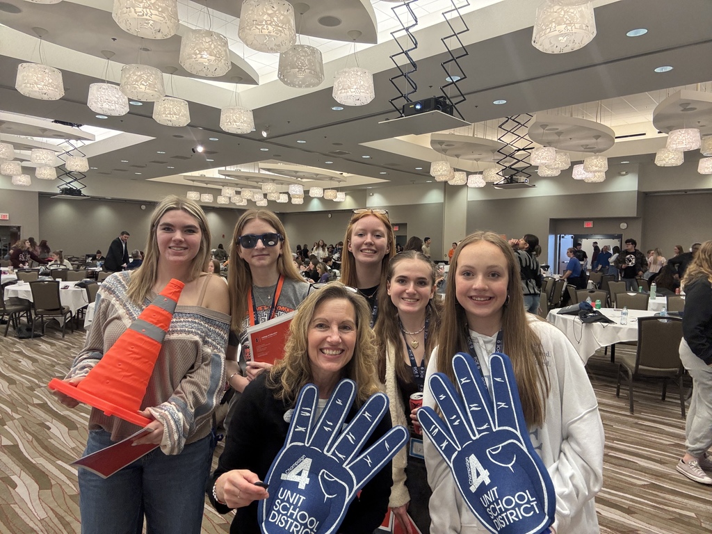 A group of women in a conference room with orange traffic cones, holding hands shaped like fingers.