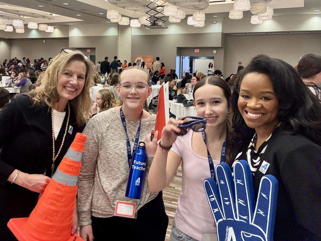 Four people in a room pose for a photo. They hold items like an orange cone, a bottle, and a glove.