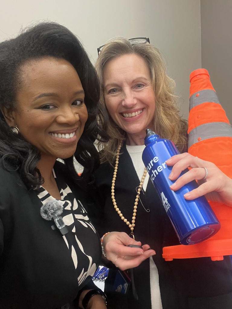 Two women smiling and posing for a photo. One holds a blue bottle, the other an orange traffic cone.