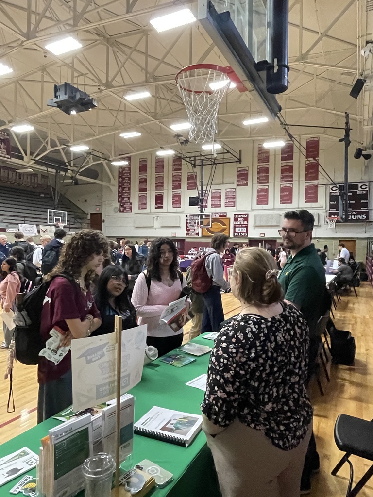 Several people gather around a table with materials in an indoor basketball court with red banners on the wall.