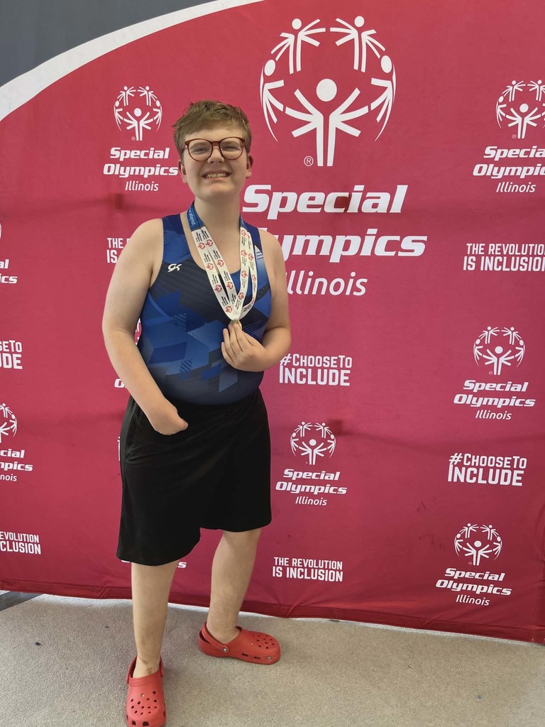 Person in blue top and glasses stands in front of a red backdrop with "Special Olympics Illinois" logo.