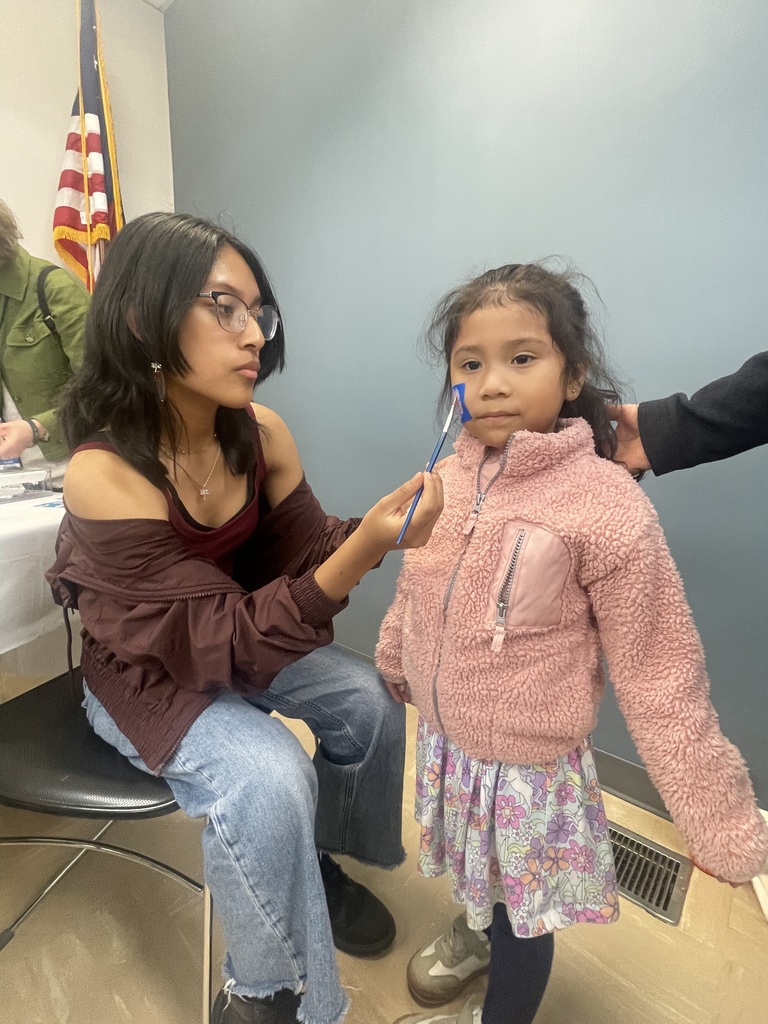 Woman with glasses checks a young girl's teeth with a dental instrument in a room.