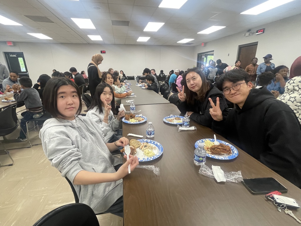 Group of people seated at tables in a dining hall, smiling and posing for a photo.