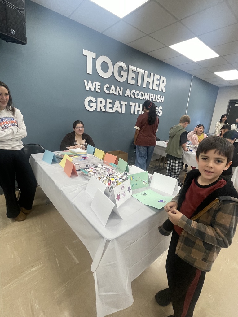 Indoor event with a blue wall. "Together we can accomplish great things" on the wall. Boy standing by a table with cards and crafts.