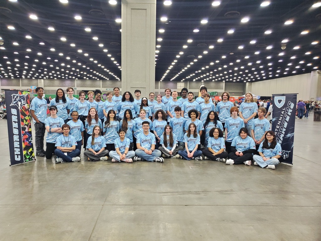 Large group of people in blue shirts posing for a photo in a brightly lit indoor venue.