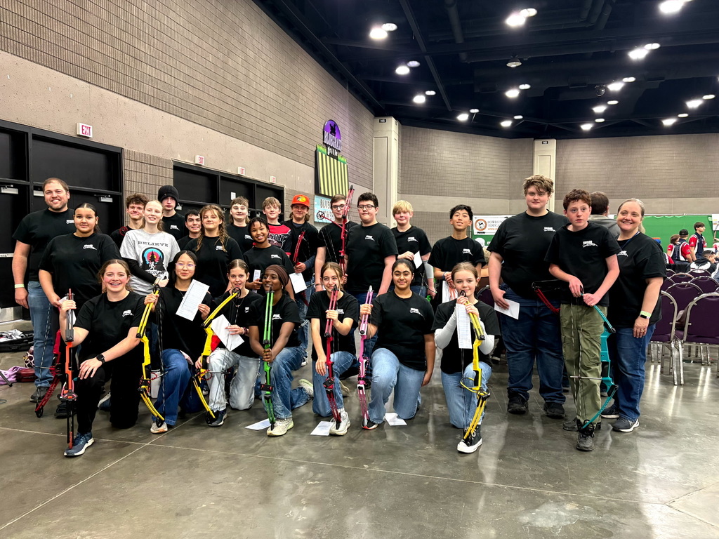 Group of people in matching black shirts and sneakers pose for photo in a large indoor venue.
