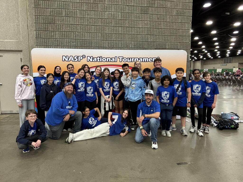 A group of people wearing blue shirts and sneakers pose for a picture in front of a banner.