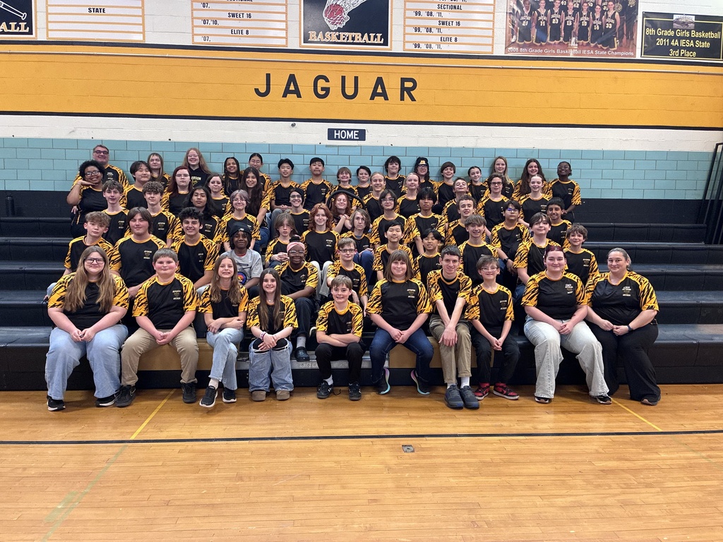 A group of people in black and yellow uniforms, likely a sports team, pose for a photo in a gym.