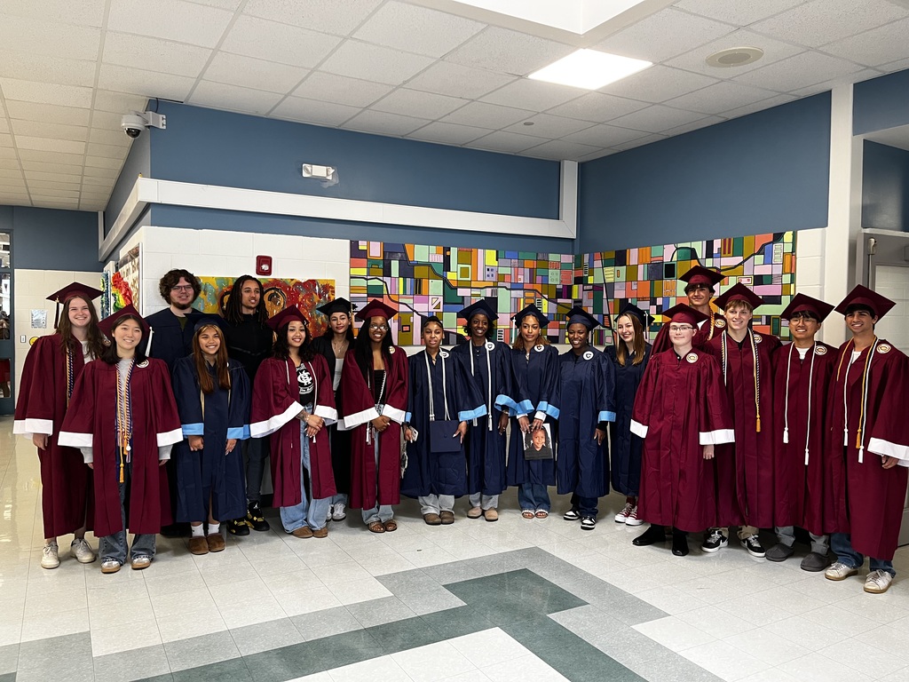 A group of students in graduation robes, smiling, pose for a photo in a school hallway.